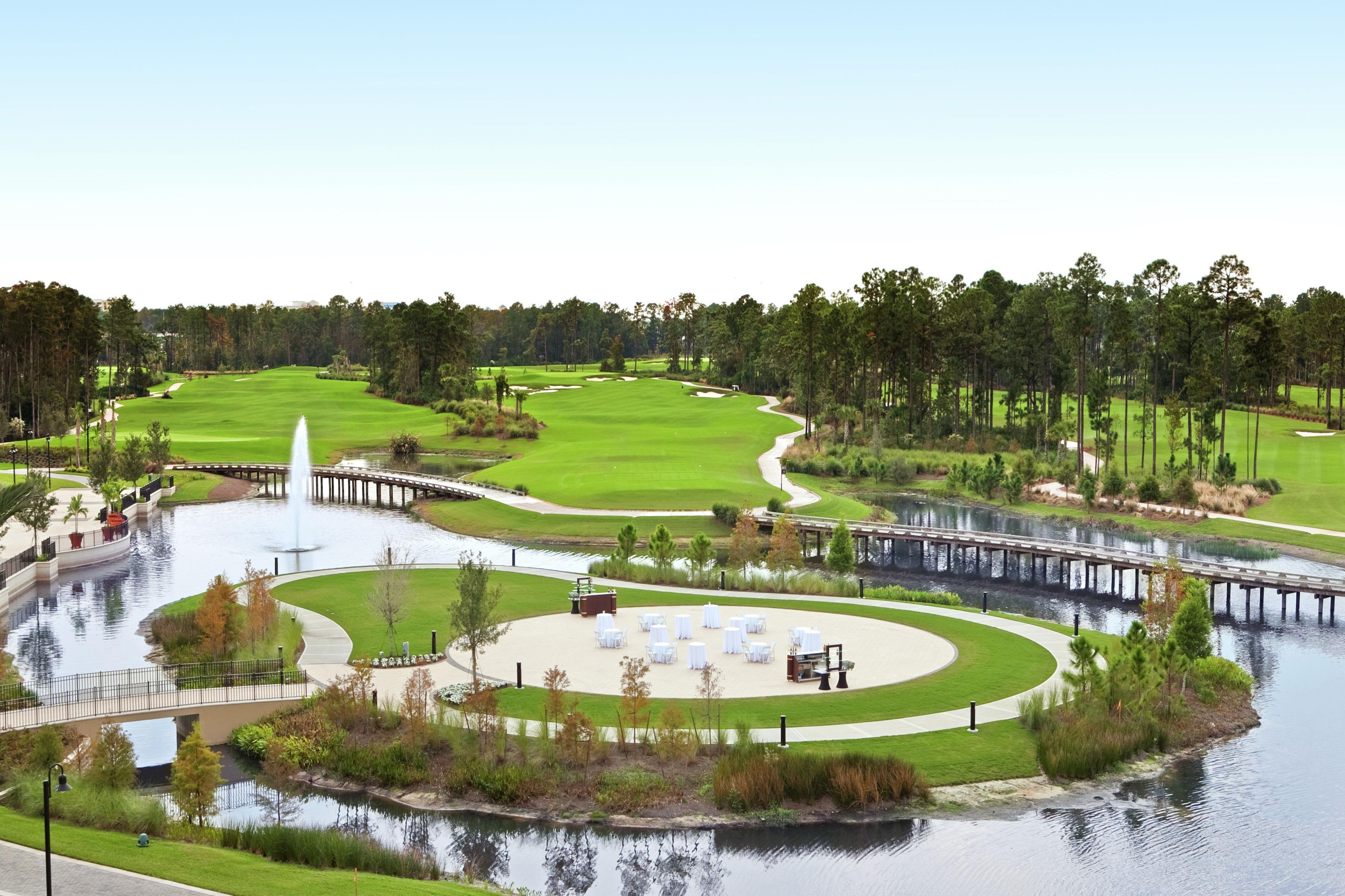 Um campo de golfe com lago, um pavilhão e uma ponte.