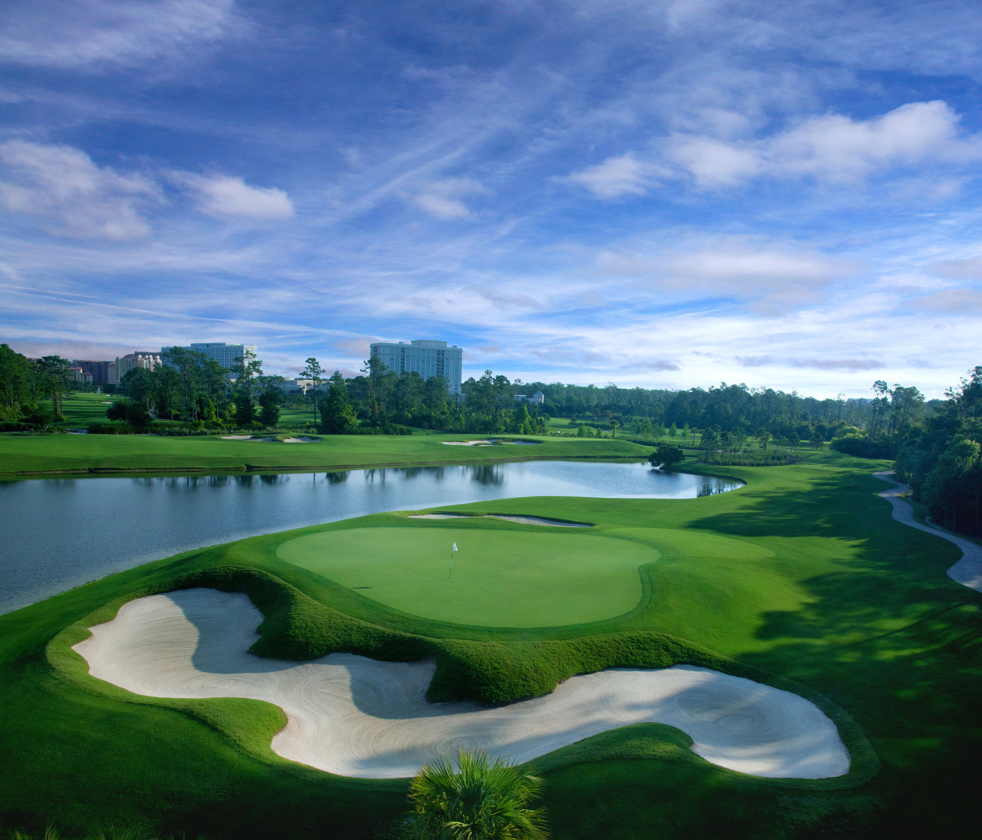 A golf course with sand bunkers, a pond, and a clear sky.