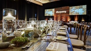 Una mesa de banquete dispuesta con cristalería, platos y un menú, con un escenario de fondo y un letrero que dice 'Signia Hilton'.