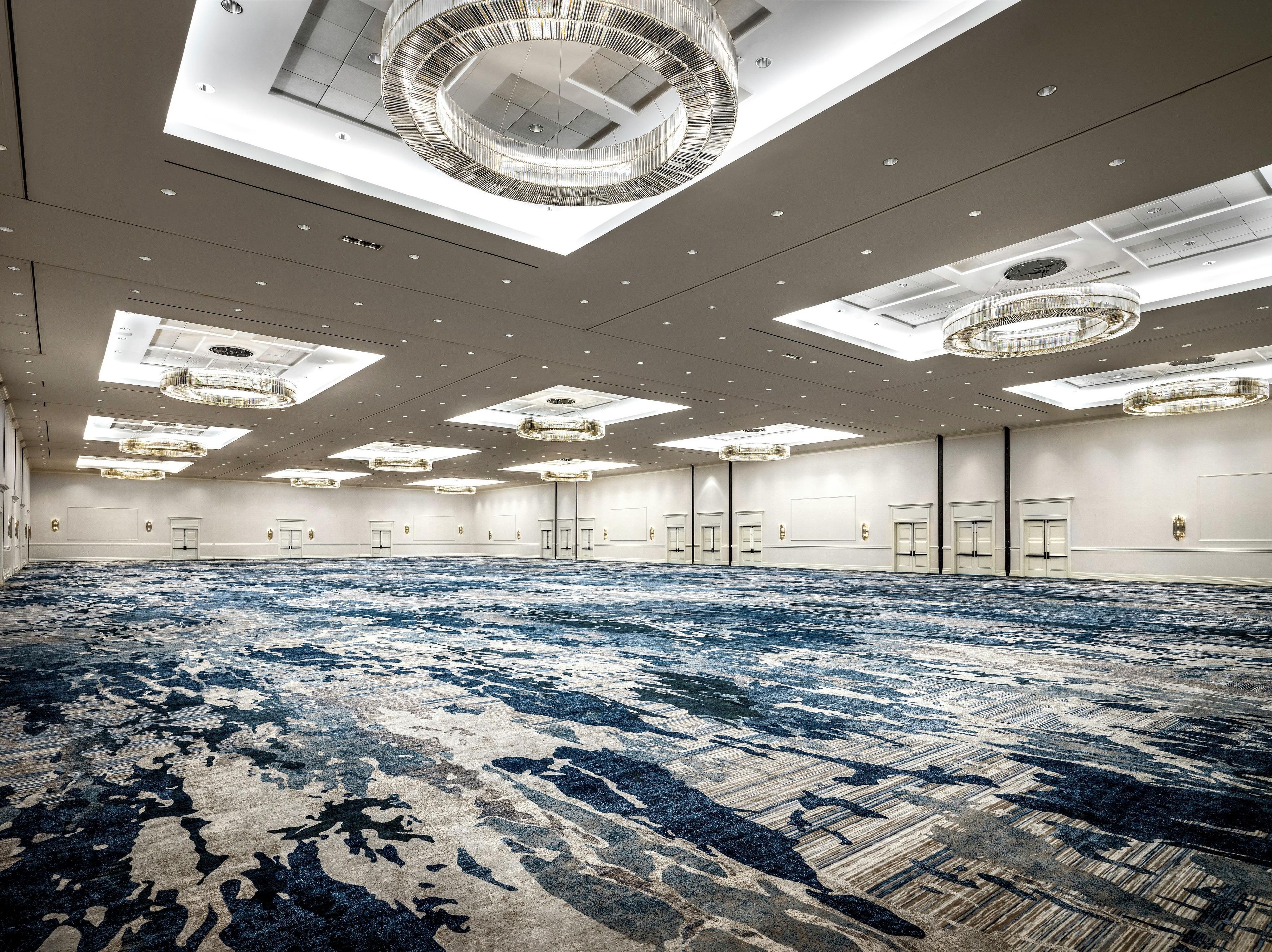 A large conference room with a patterned carpet, multiple doors, and modern ceiling lights.