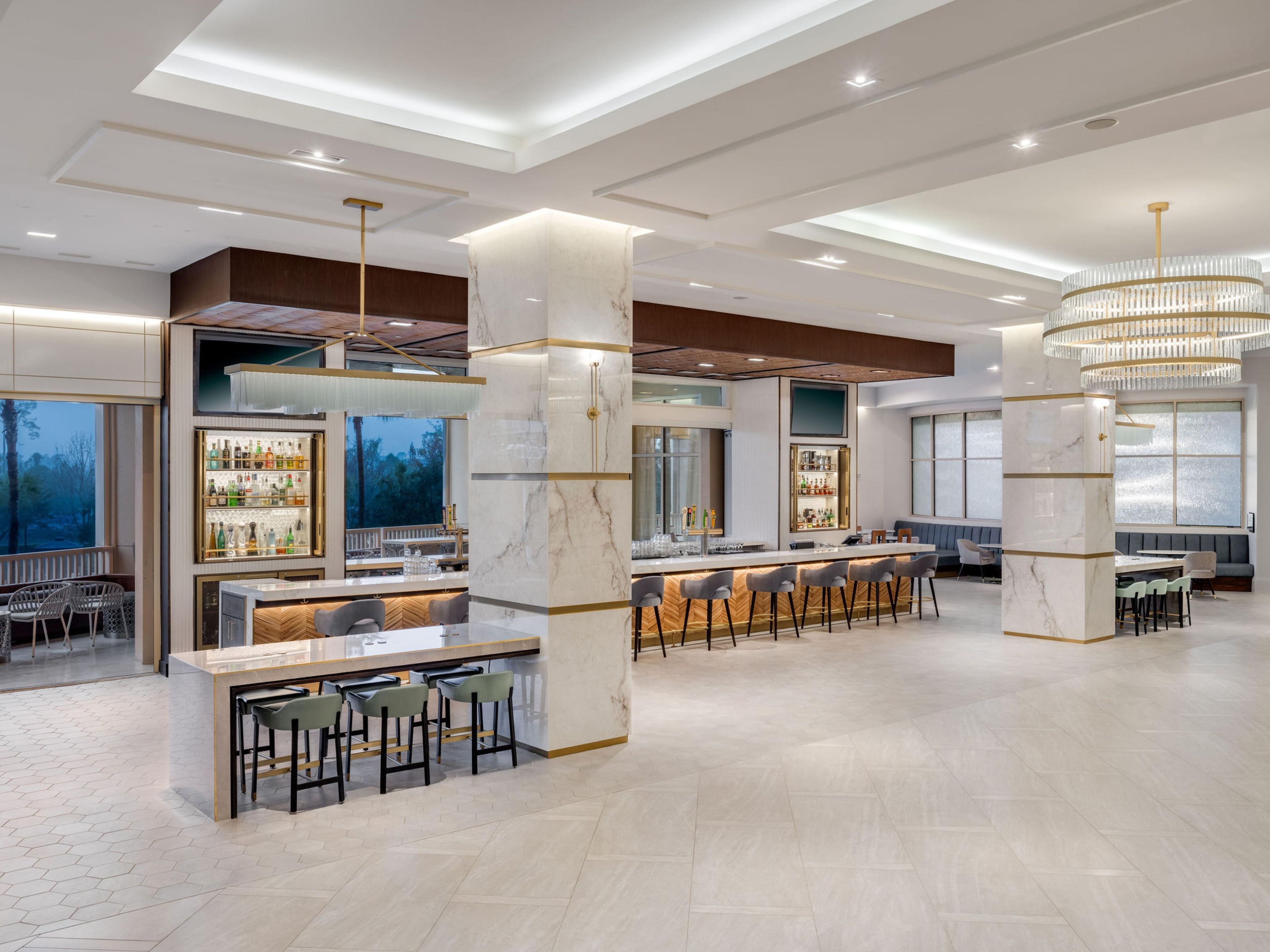 Uma área de bar moderna com colunas de mármore, banquetas e um grande candelabro.