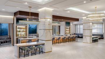 Uma área de bar moderna com colunas de mármore, banquetas e um grande candelabro.