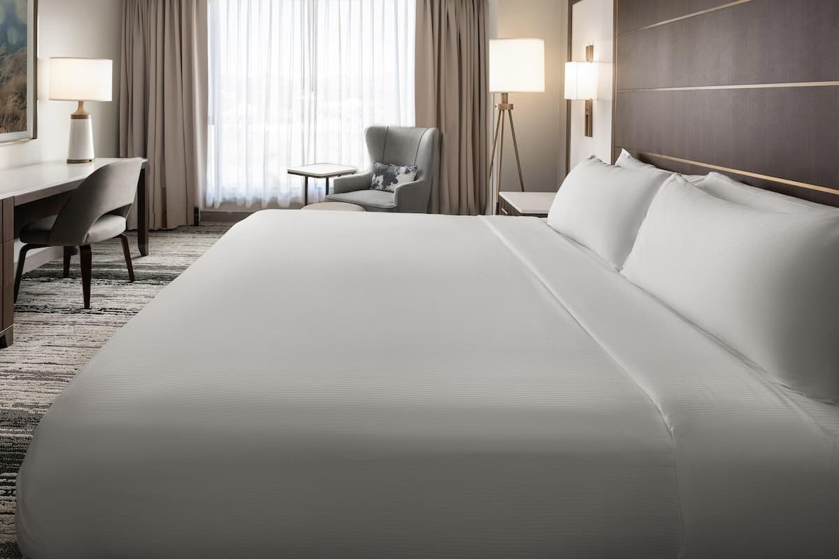 Ein Hotelzimmer mit einem großen Bett, einem Schreibtisch, einem Stuhl, einem kleinen Tisch und einer Stehlampe.