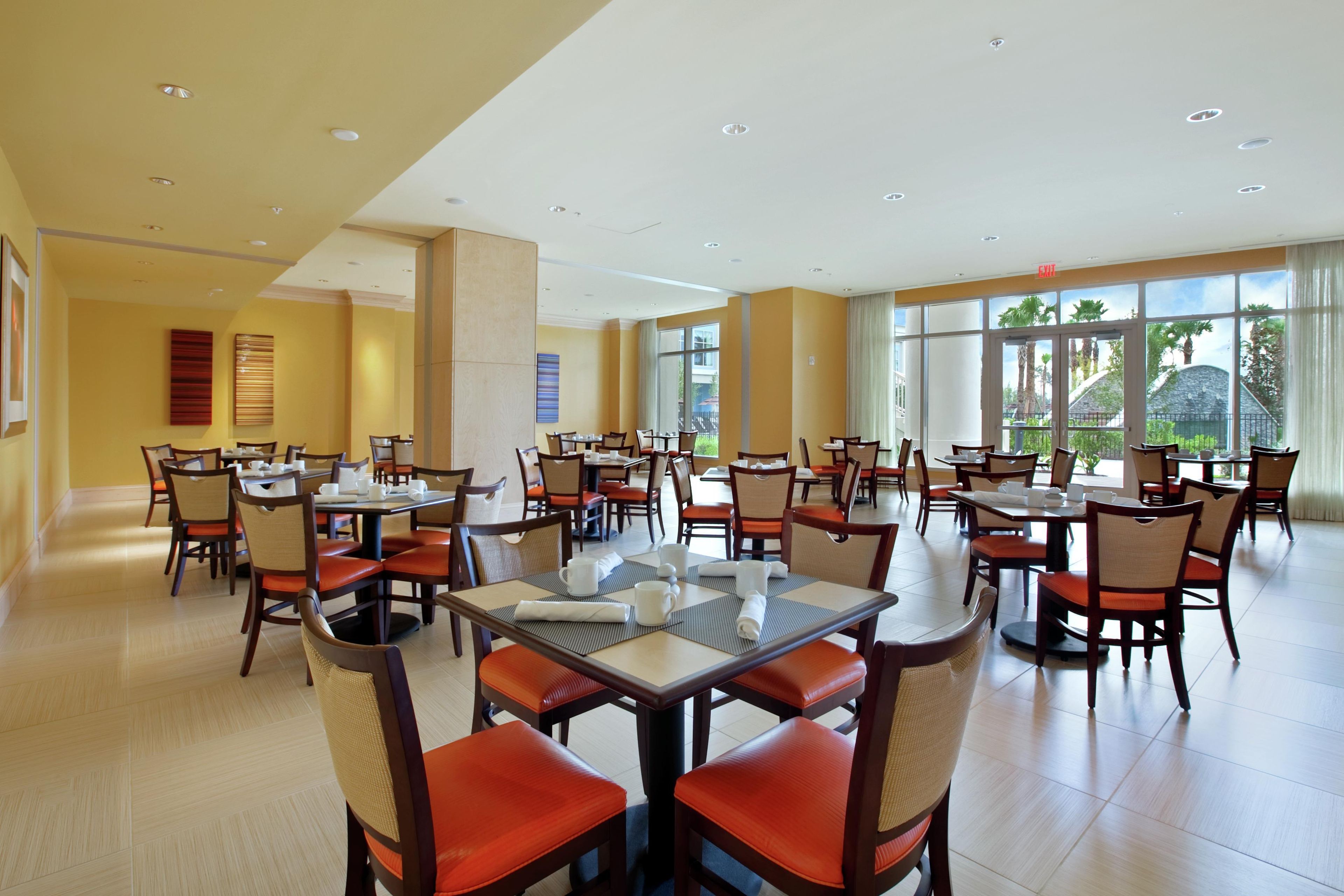 Un vaste espace dédié à la salle à manger, avec de nombreuses tables et chaises, de grandes fenêtres et un aménagement épuré et moderne.