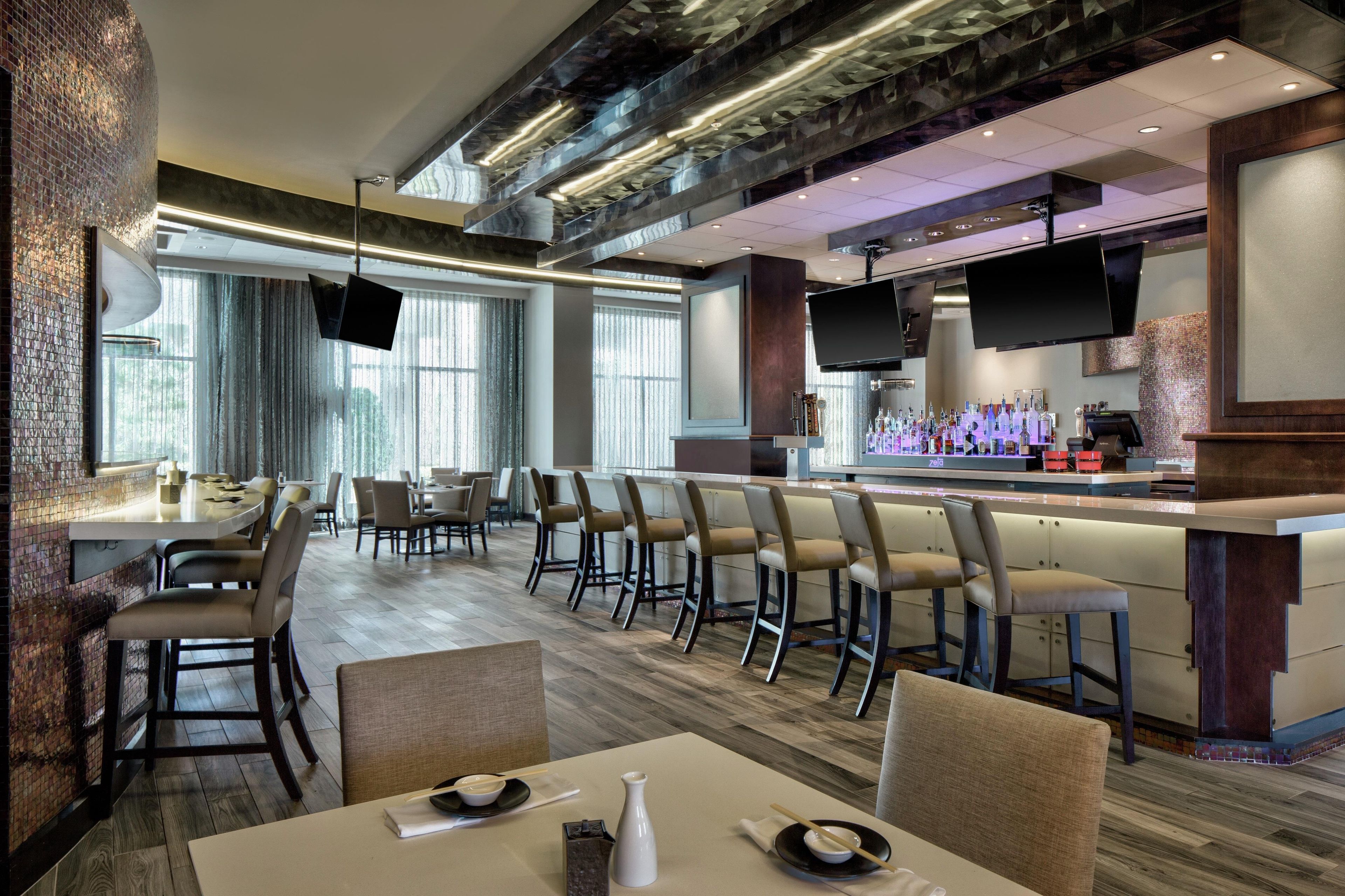 A modern restaurant with a bar area, multiple seating options, and a television screen.