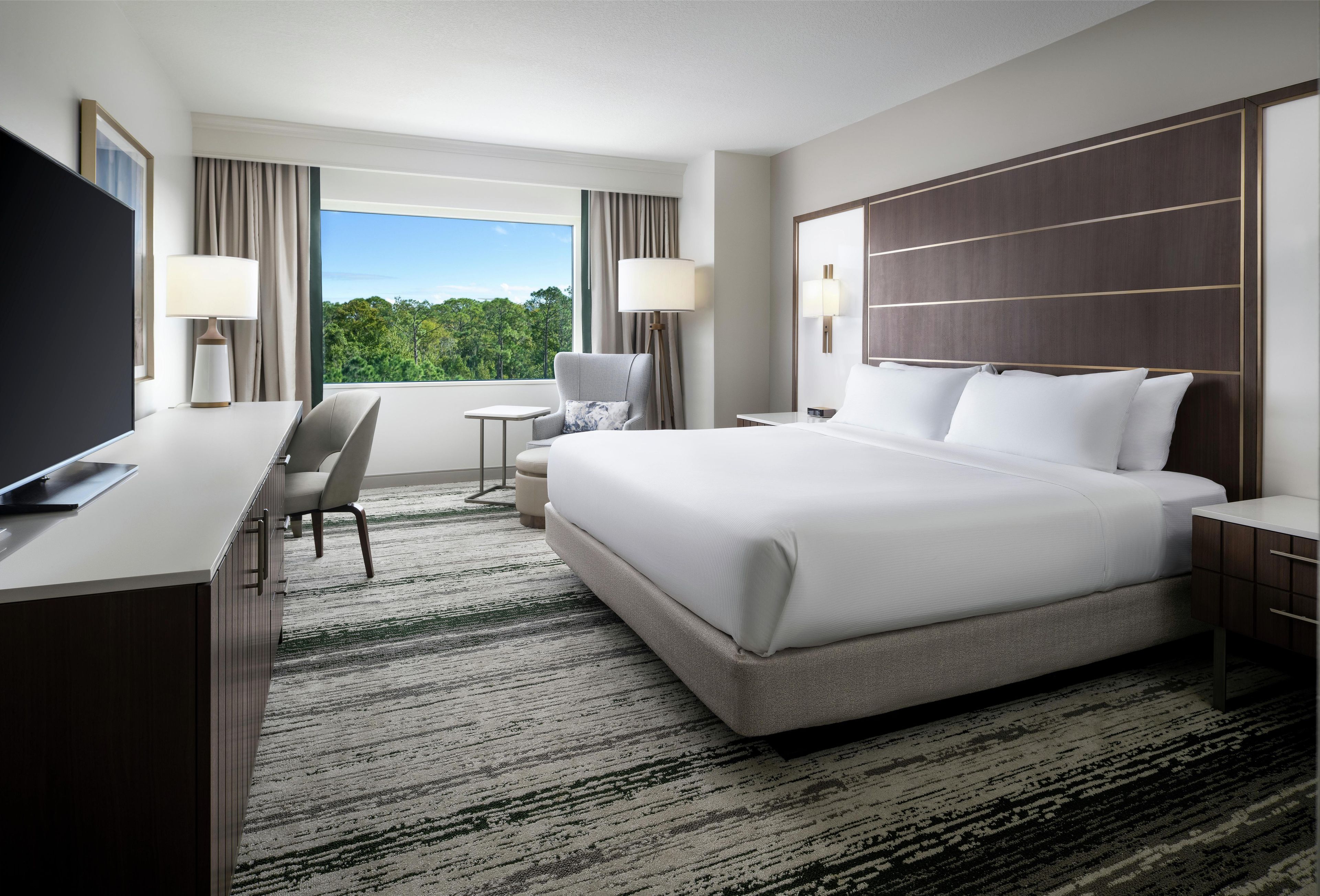 Habitación de hotel con cama, escritorio, silla y televisor.