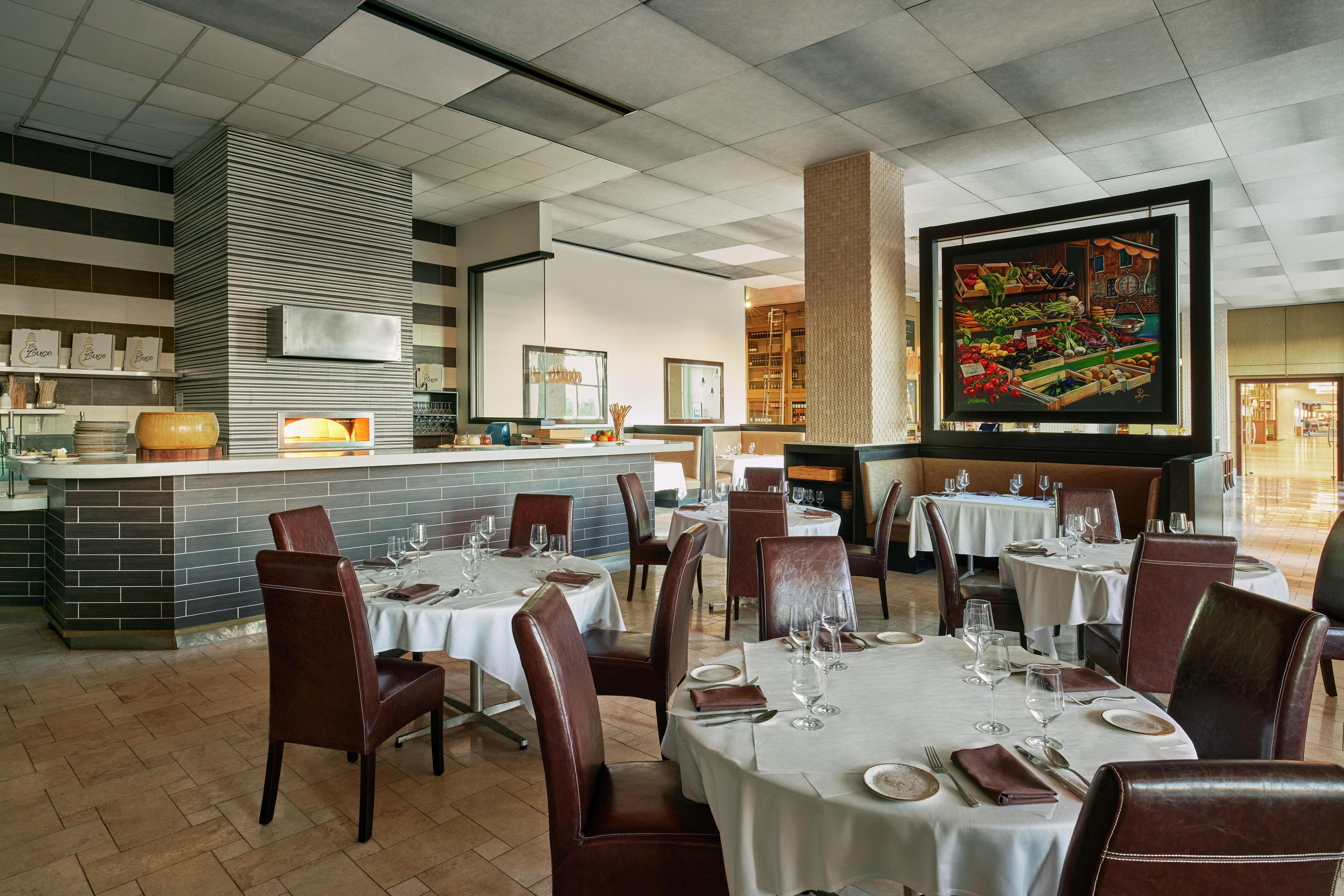 Un restaurant avec des tables dressées pour le service, un coin bar et un grand tableau accroché au mur.