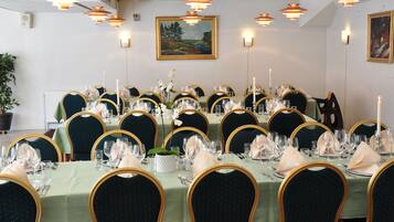 A dining area with round tables set for a meal, featuring green tablecloths, gold chairs, and candle centerpieces.