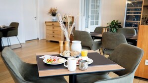 A dining area with a table set for breakfast, including plates of food, a coffee mug, and a glass of orange juice. There are chairs around the table, and a plant is visible in the background. - Vildbjerg Hotel (Vildbjerg)