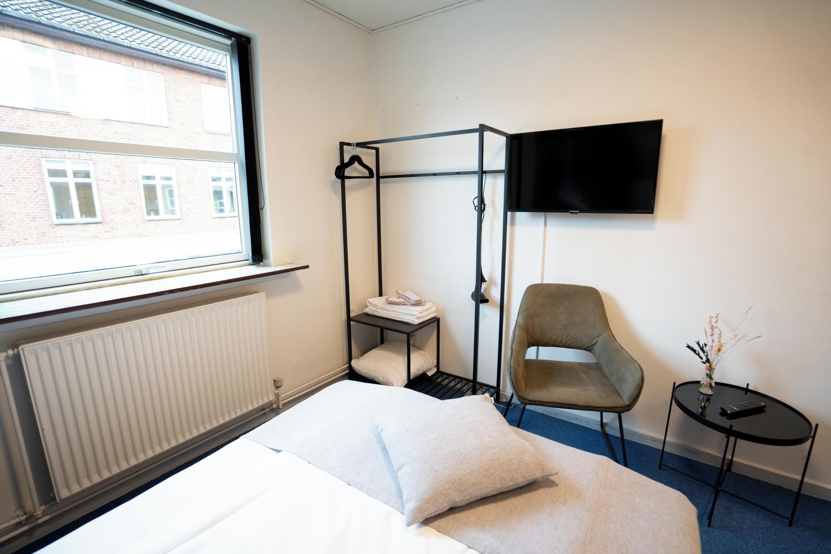 A hotel room with a bed, a chair, a small table, a TV, and a window with a view of buildings.