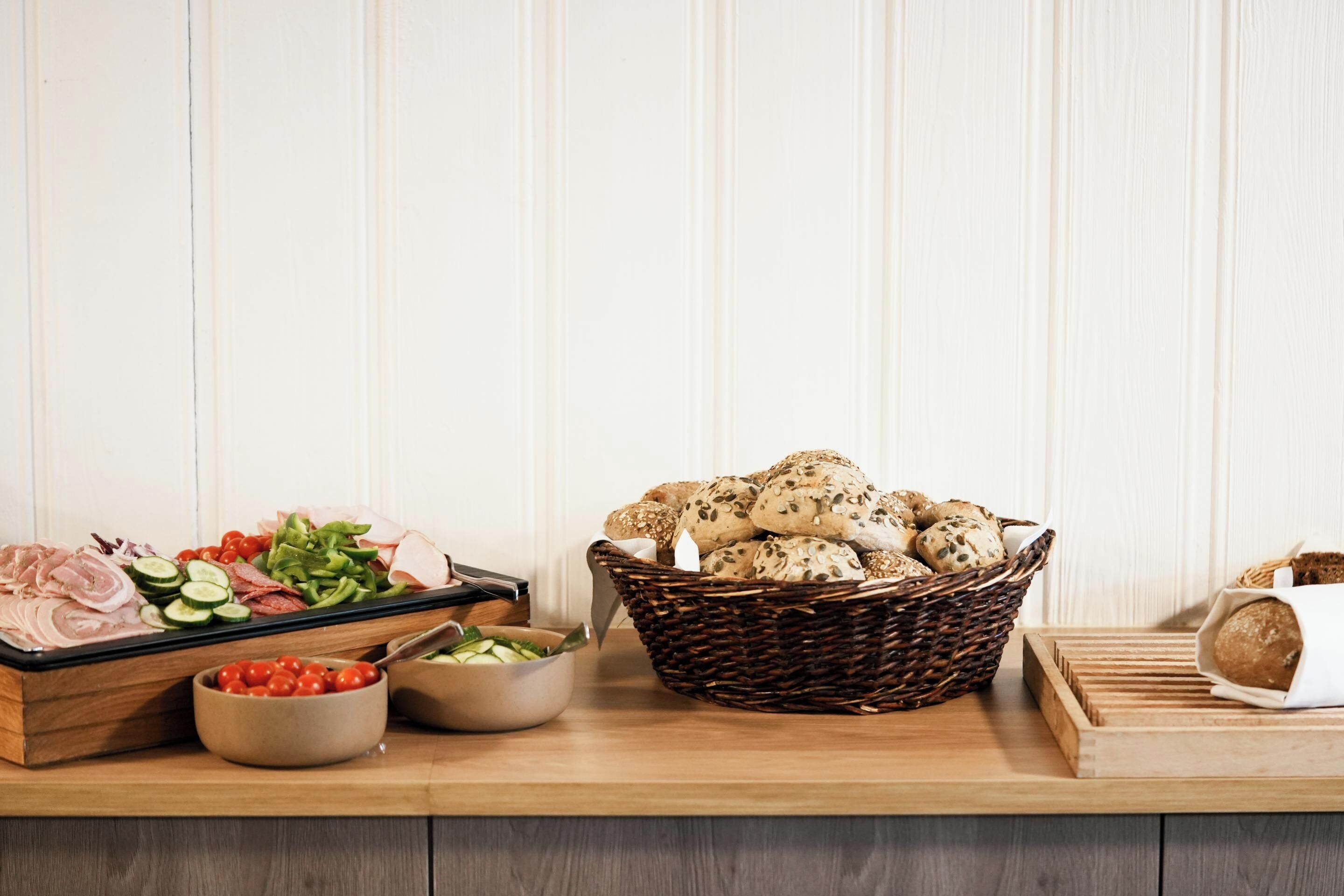 Ein Holztisch mit verschiedenen Speisen, darunter Aufschnitt, Gemüse und Brot.