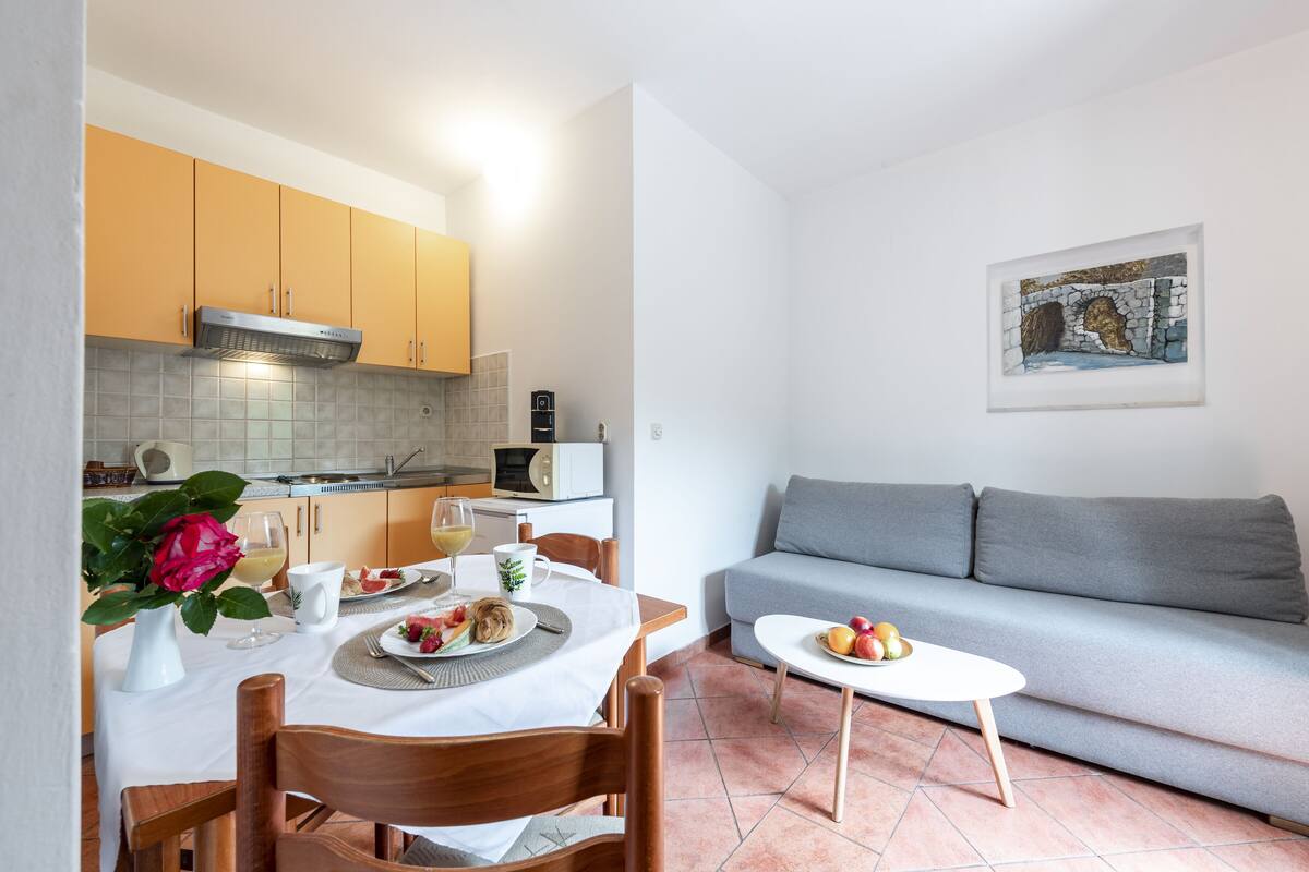 A compact living space with a dining area, kitchenette, and a gray sofa.