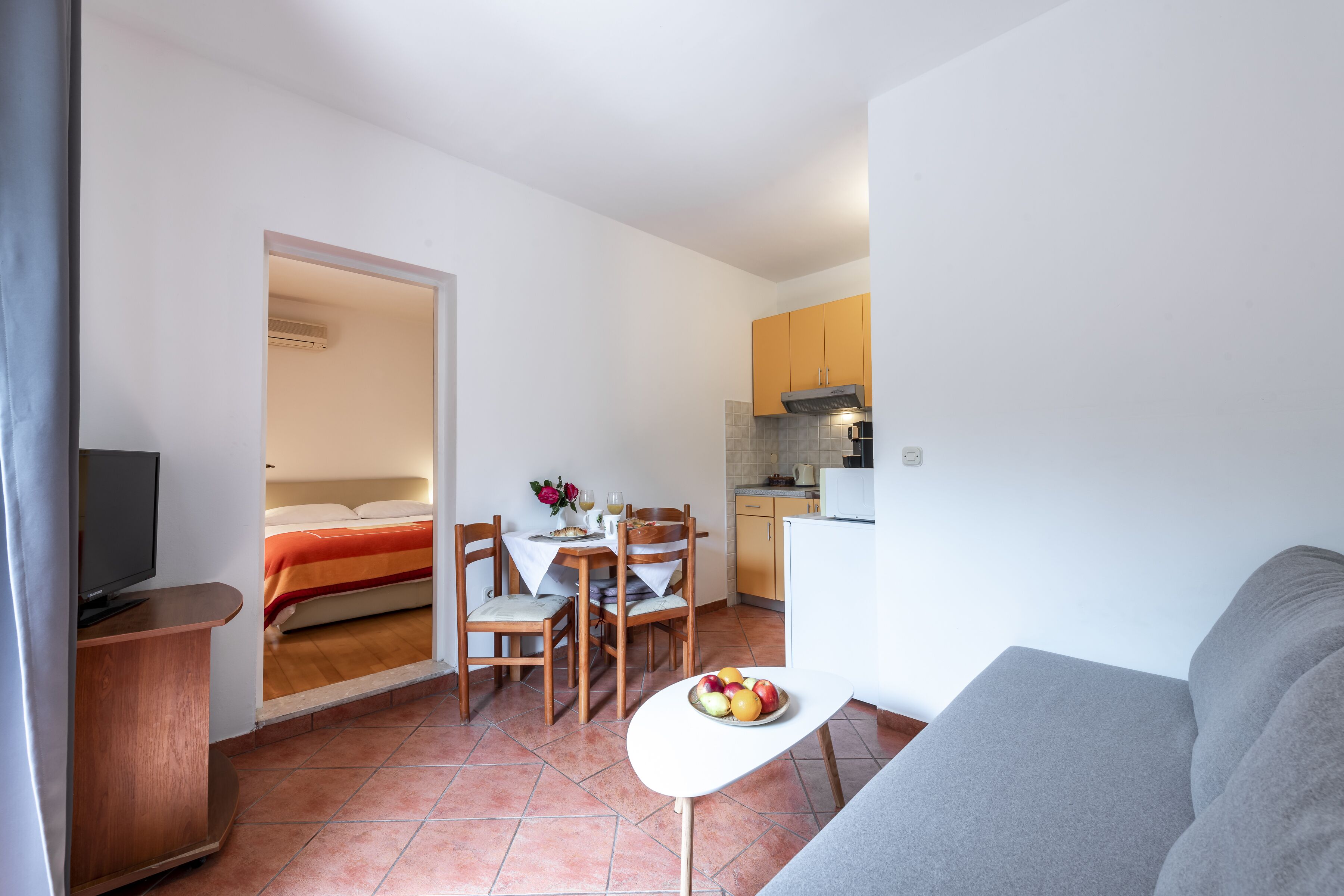 A compact living space with a kitchenette, a dining area, and a seating area with a TV and a fruit bowl.