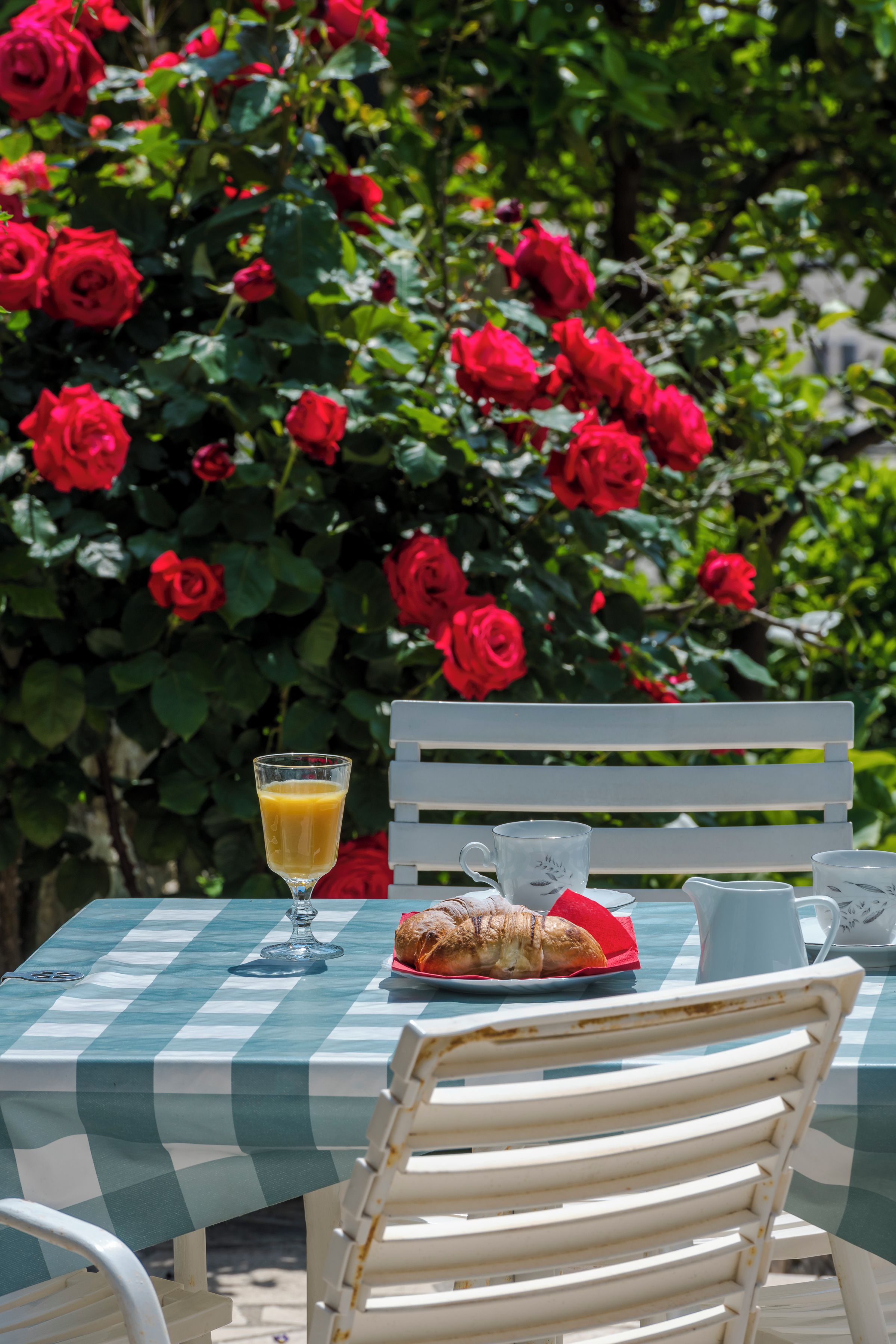 A table with a checkered tablecloth, a glass of orange juice, a croissant, a pitcher, and a cup.