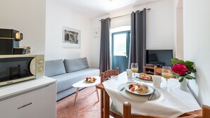 A compact living space with a kitchenette, a dining area, a sofa, a TV, and a window with curtains. - Villa Doris (Dubrovnik)