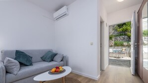 A modern living room with a grey sofa, a small round table with fruit, and a view to an outdoor patio area. - Villa Doris (Dubrovnik)