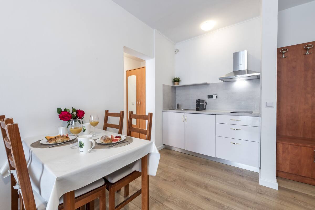 A modern kitchen with white cabinets, a stainless steel range hood, and a dining area with a table set for two.