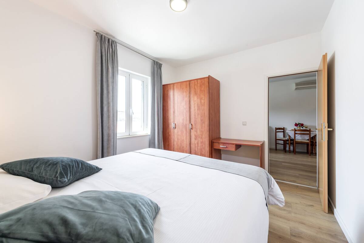 A bedroom with a bed, a wooden wardrobe, a desk, and a mirror.