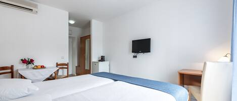 Habitación de hotel con dos camas, un escritorio, una silla, un televisor y una mesita con flores y fruta.