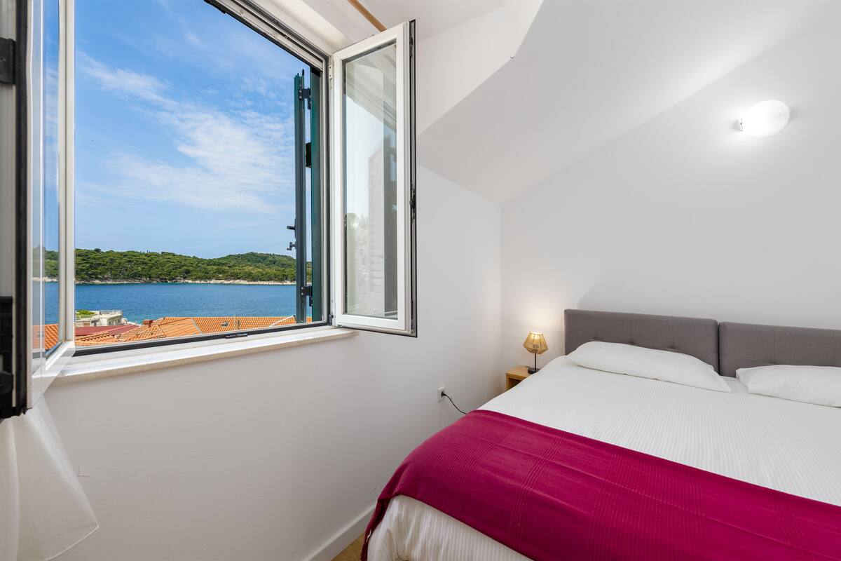 A bedroom with a large window offering a view of a body of water and greenery.