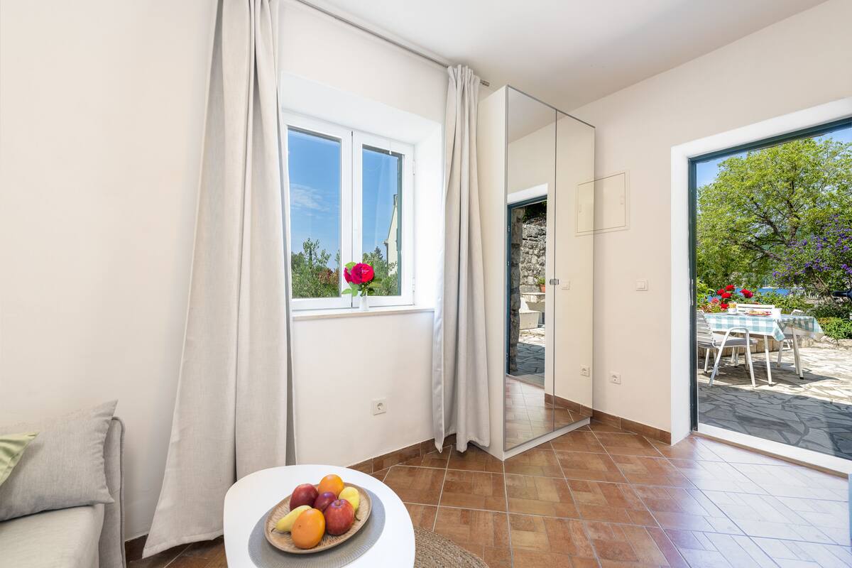A modern room with a large window, a dining area with a table and chairs, and a fruit bowl on a small table.