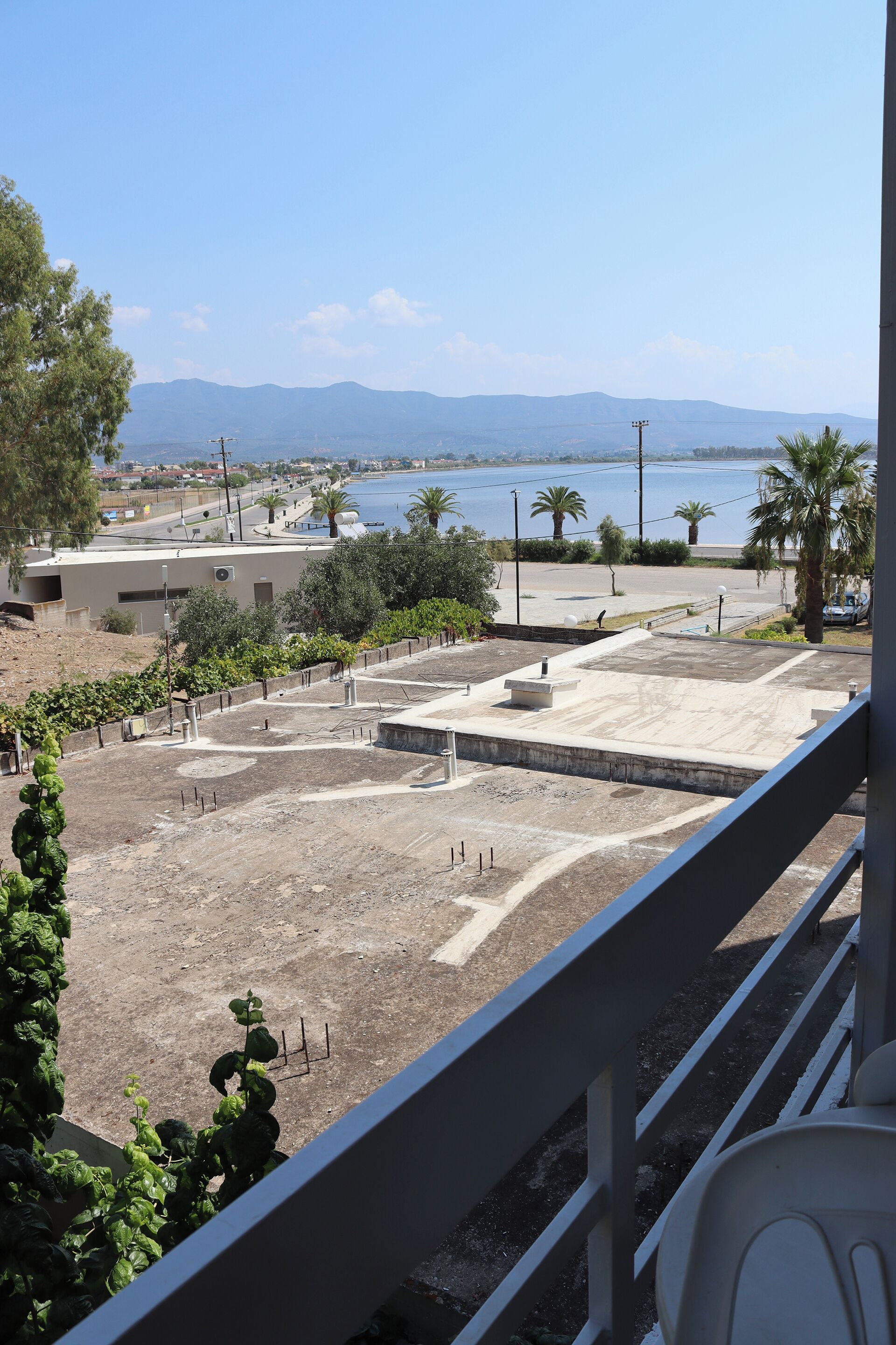 A view from a balcony overlooking a landscaped area with a pool, palm trees, and distant mountains.