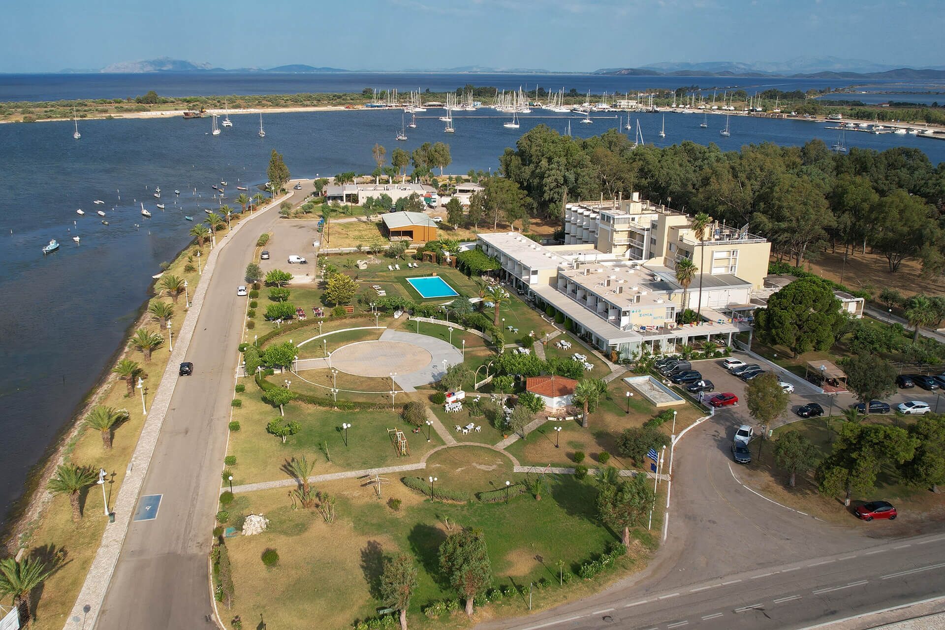 Ein Luftbild einer Küstenimmobilie mit Schwimmbad, Tennisplatz und einem großen Mehrstöckigen Gebäude.