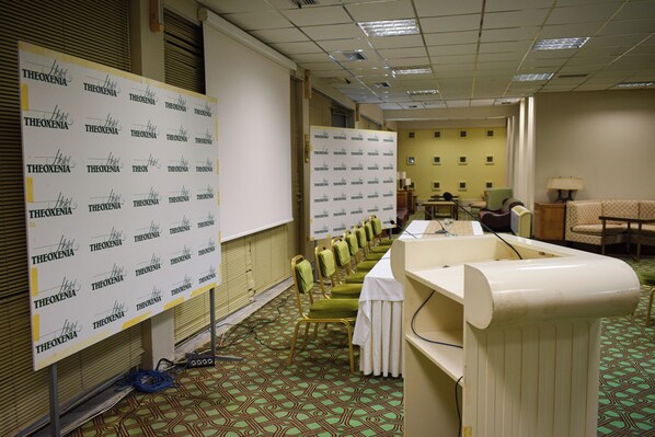 A hotel room with a conference table, chairs, a whiteboard, and a patterned carpet. - Theoxenia (Mesolongi)