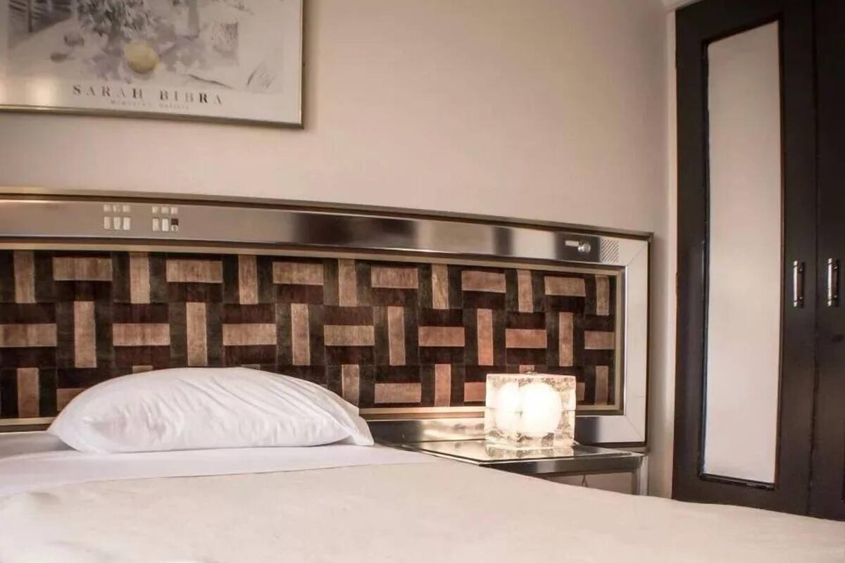 Ein Hotelzimmer mit einem Bett, einem Nachttisch, einem gerahmten Bild an der Wand und einer Tür.