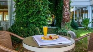 A table with a sandwich, fries, and a glass of orange juice, set outdoors with greenery and a building in the background. - Theoxenia (Mesolongi)