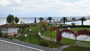 A coastal view with a white fence, palm trees, and a body of water. - Theoxenia (Mesolongi)