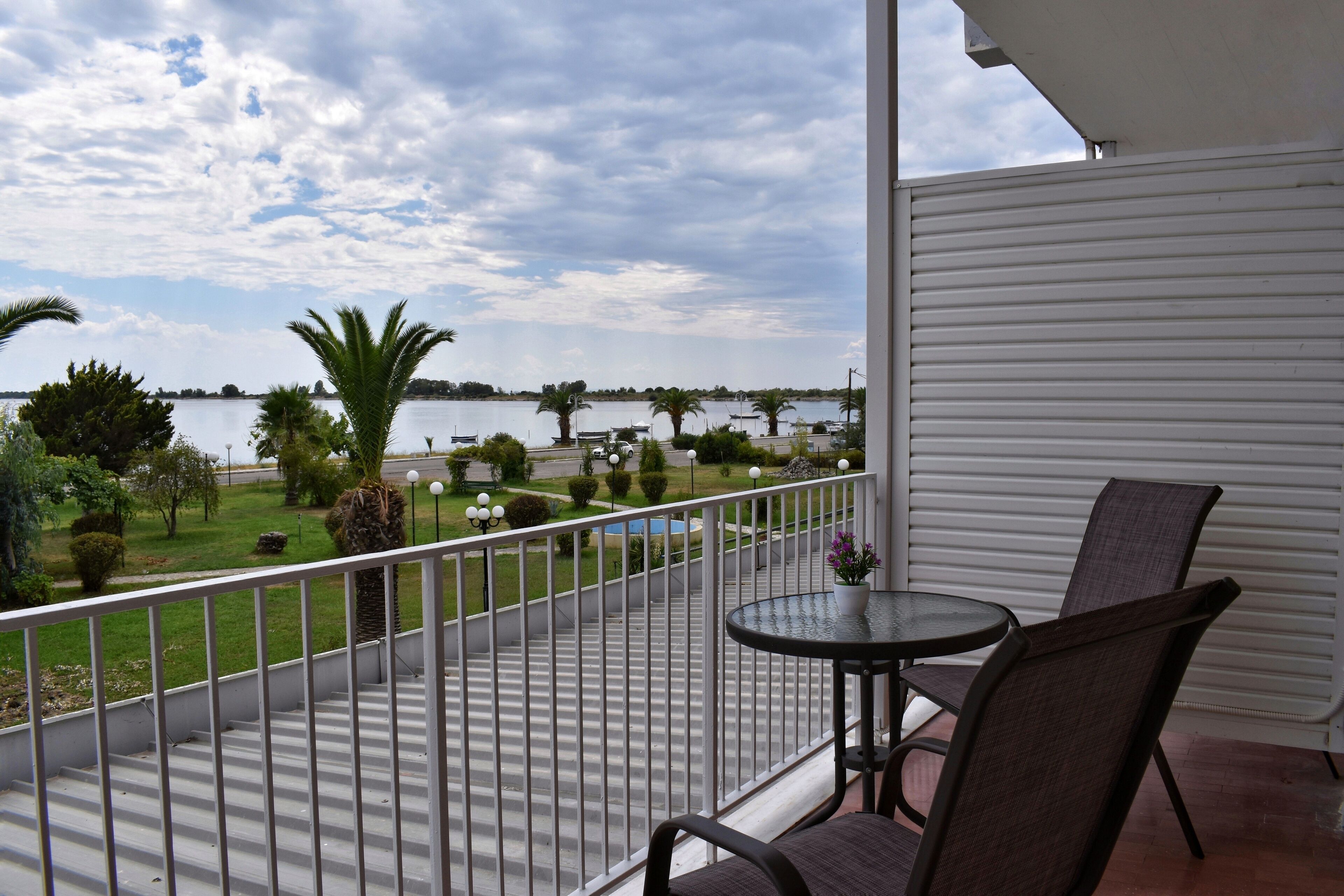 A balcony with a view of a lake, a small table, and two chairs.