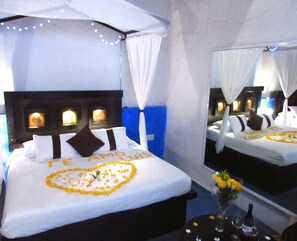 A hotel room with a bed, a bedside table with a vase of flowers, and a large mirror. - Hotel & Spa La Mansión del Burro Azul (Querétaro)