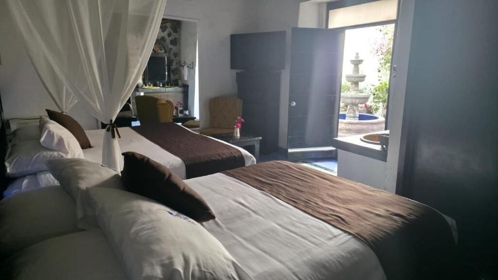 Une chambre avec deux lits, une table de chevet, une chaise et une fenêtre donnant sur une fontaine.