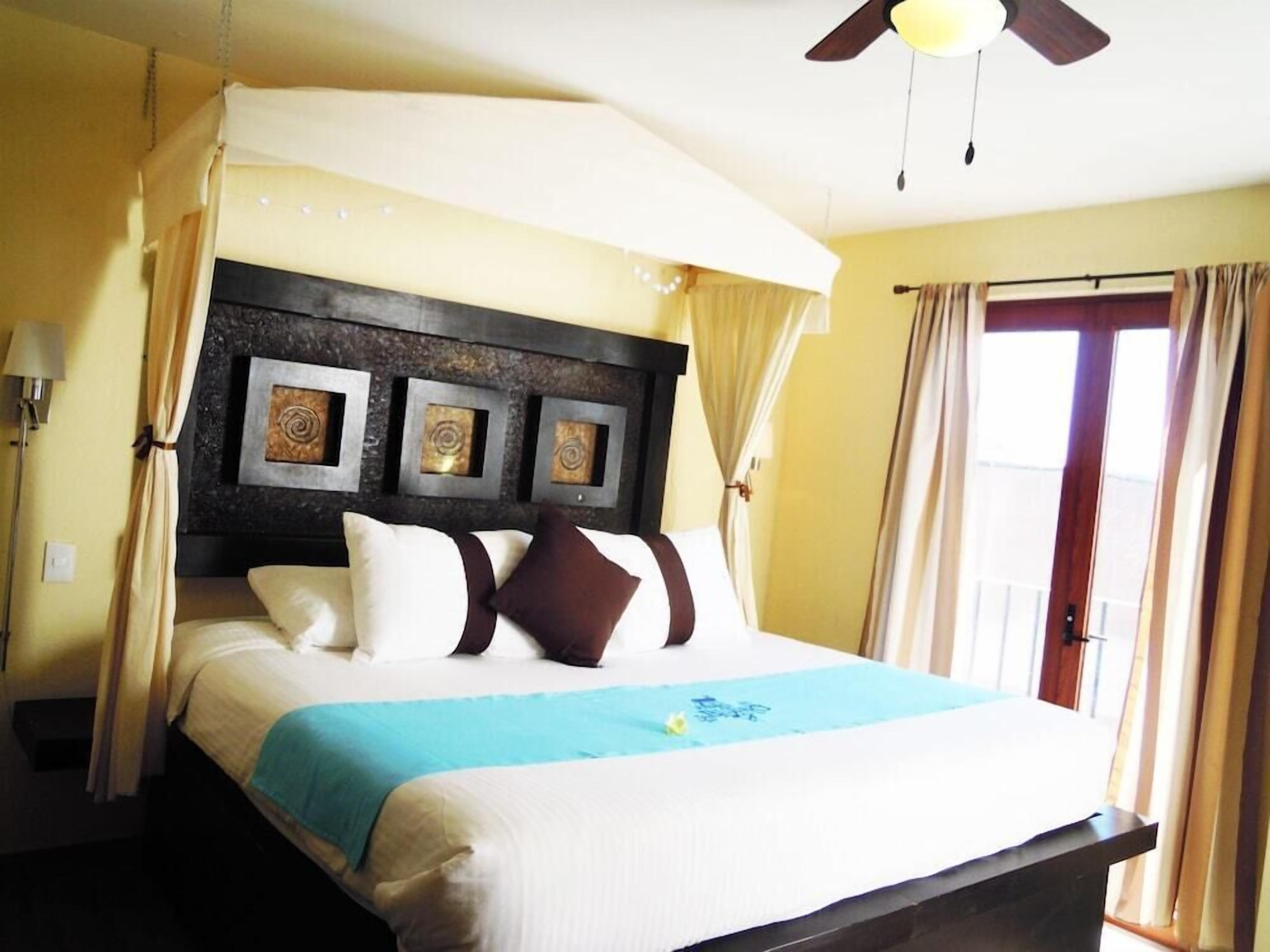 Une chambre d’hôtel avec un lit, un ventilateur de plafond et une fenêtre avec des rideaux.