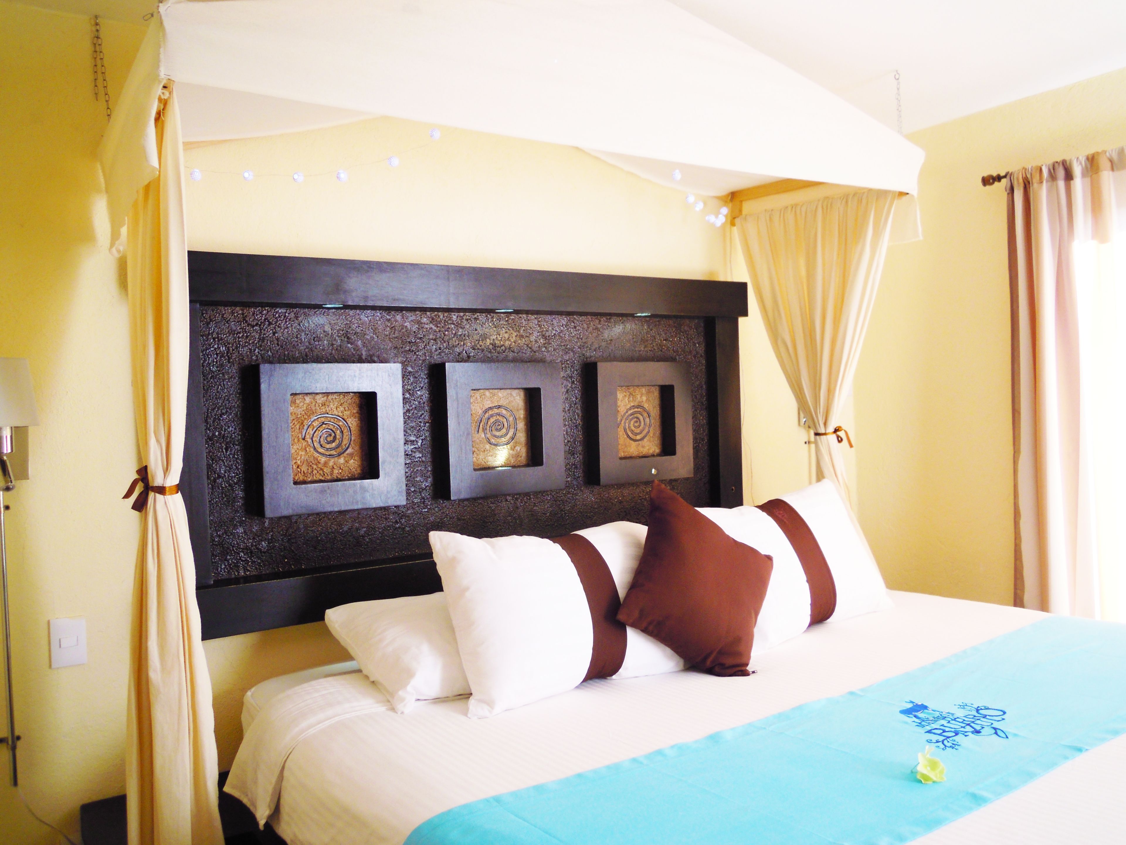 Una habitación de hotel con una cama grande, cabecera con paneles decorativos y una cortina.