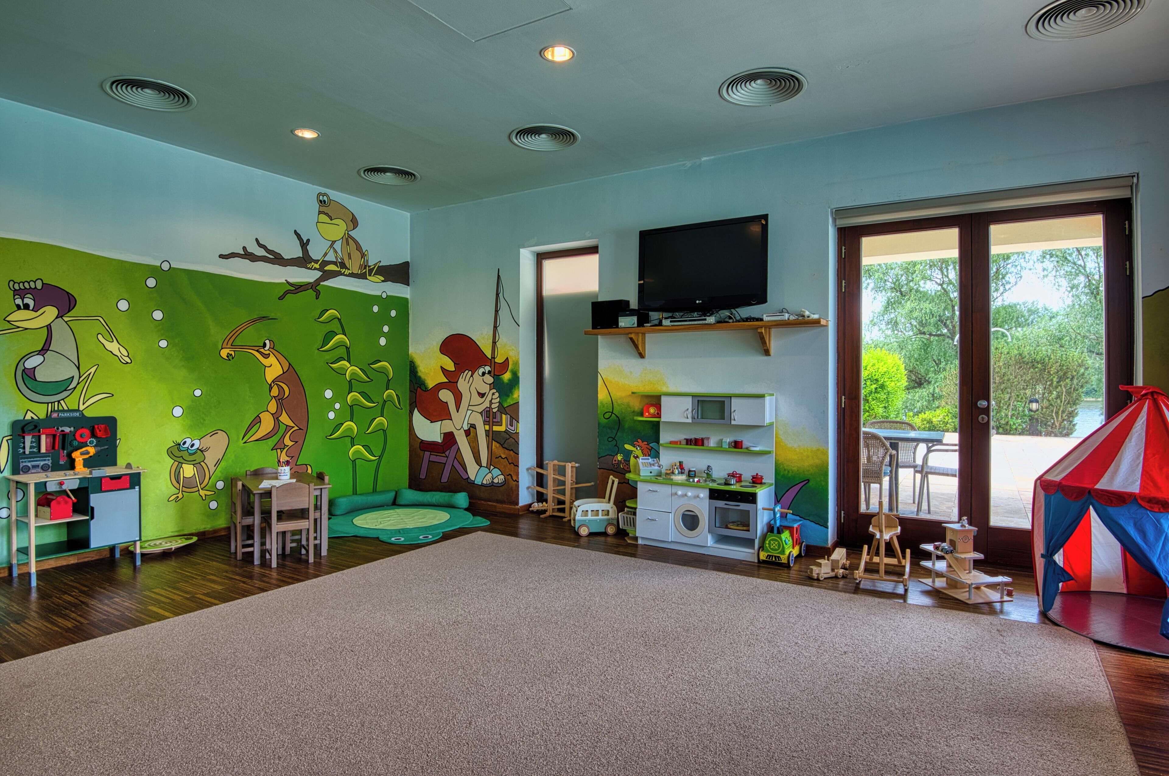 Ein Kinderspielzimmer mit einer großen Wandmalerei, einem Spielbereich und einem Fernseher.