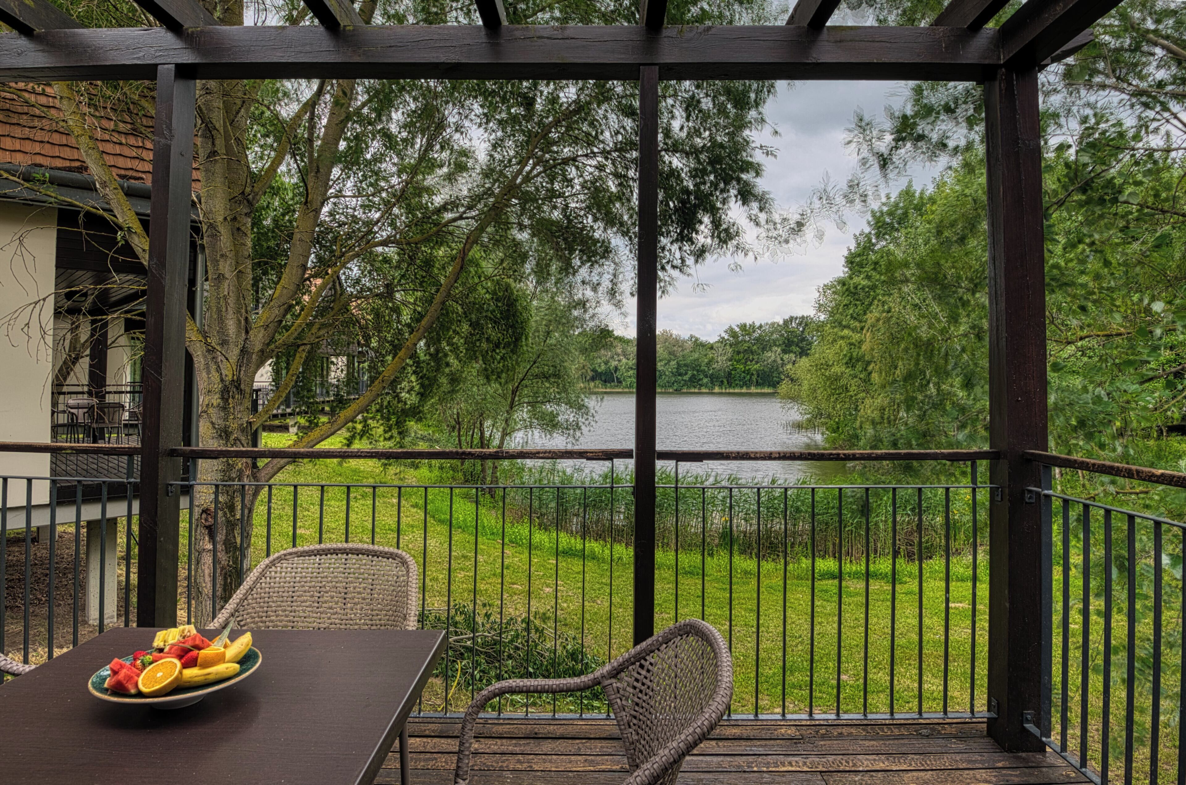 Un espace extérieur abrité, doté d’une table et de chaises, offrant une vue sur un lac et la verdure environnante.