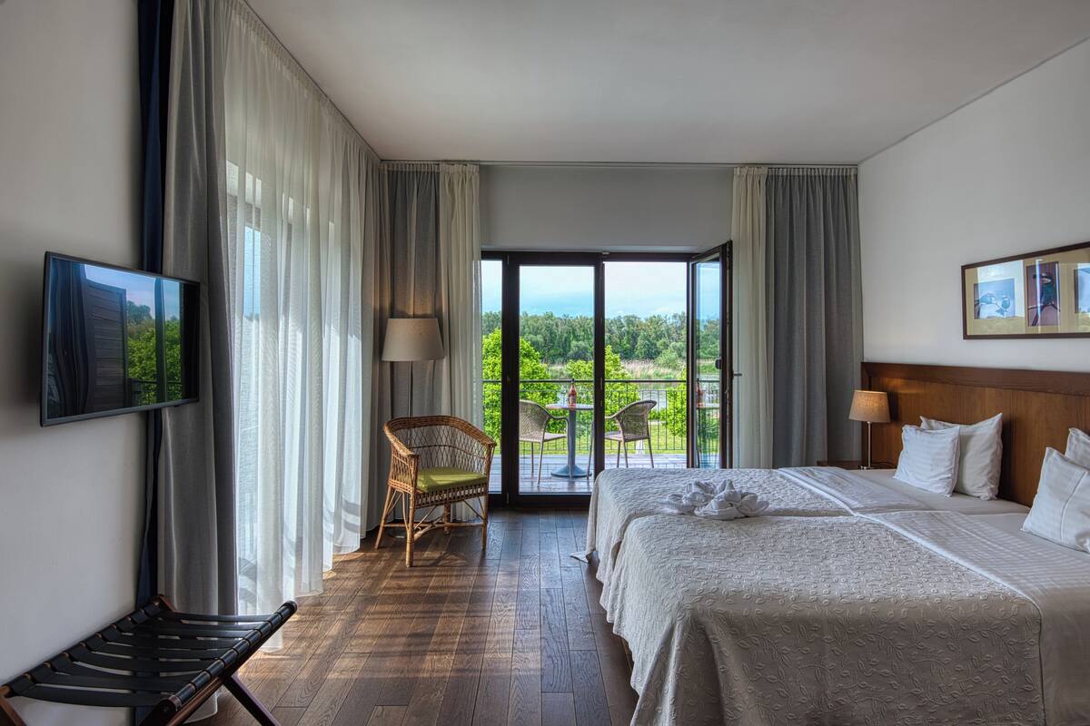 Hotelkamer met een bed, een stoel, een televisie en een balkon met een tafel en stoelen.