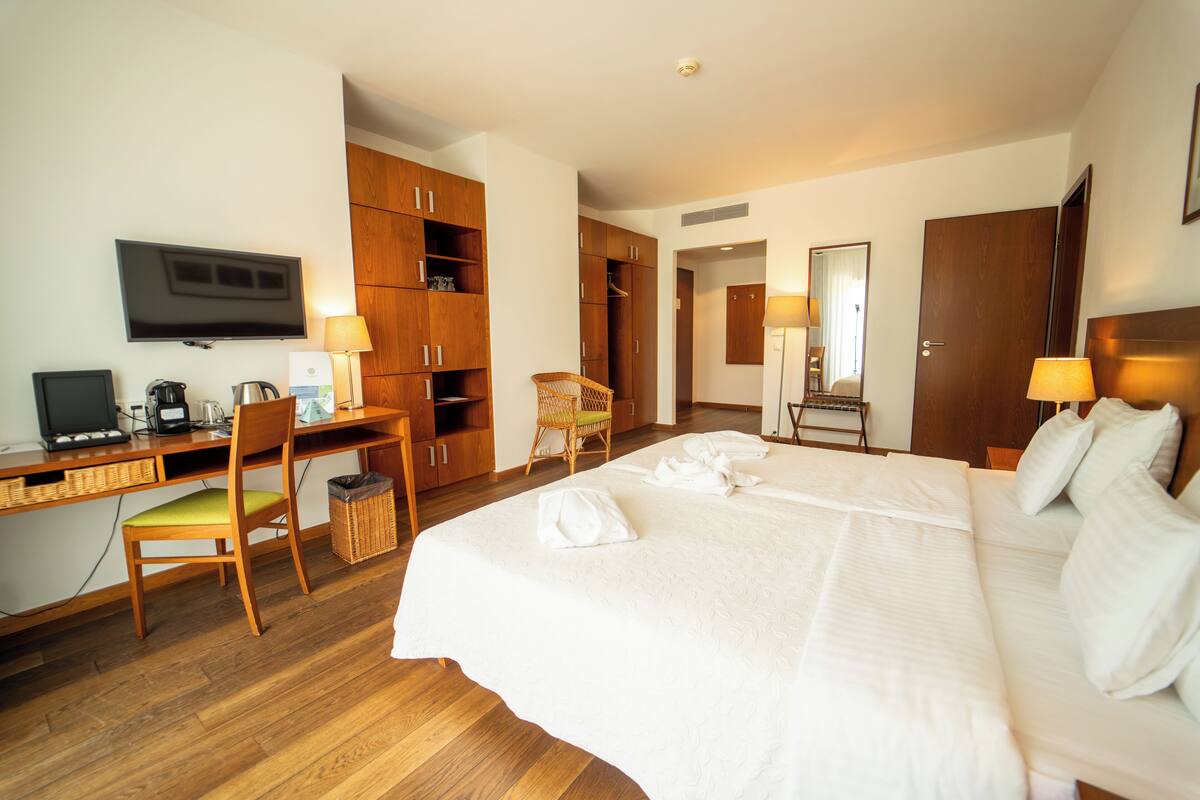 Een hotelkamer met een bed, een bureau met een computer, een stoel, een televisie en houten kasten.