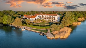 A large, multi-story building with a courtyard, surrounded by trees and a body of water. - Tisza Balneum Thermal Hotel (Tiszafured)