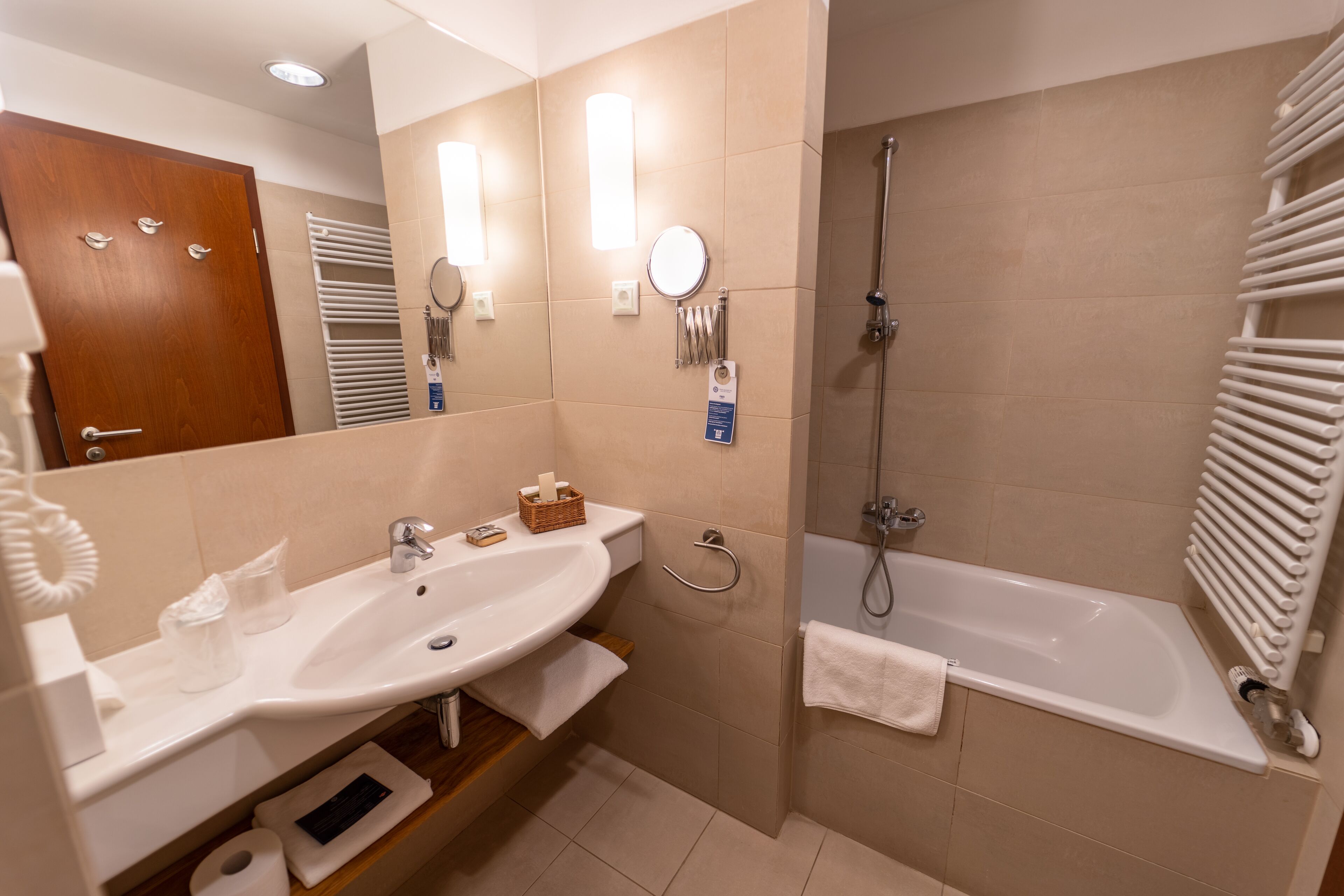 A modern bathroom with a sink, mirror, towel rack, shower, and a white radiator.