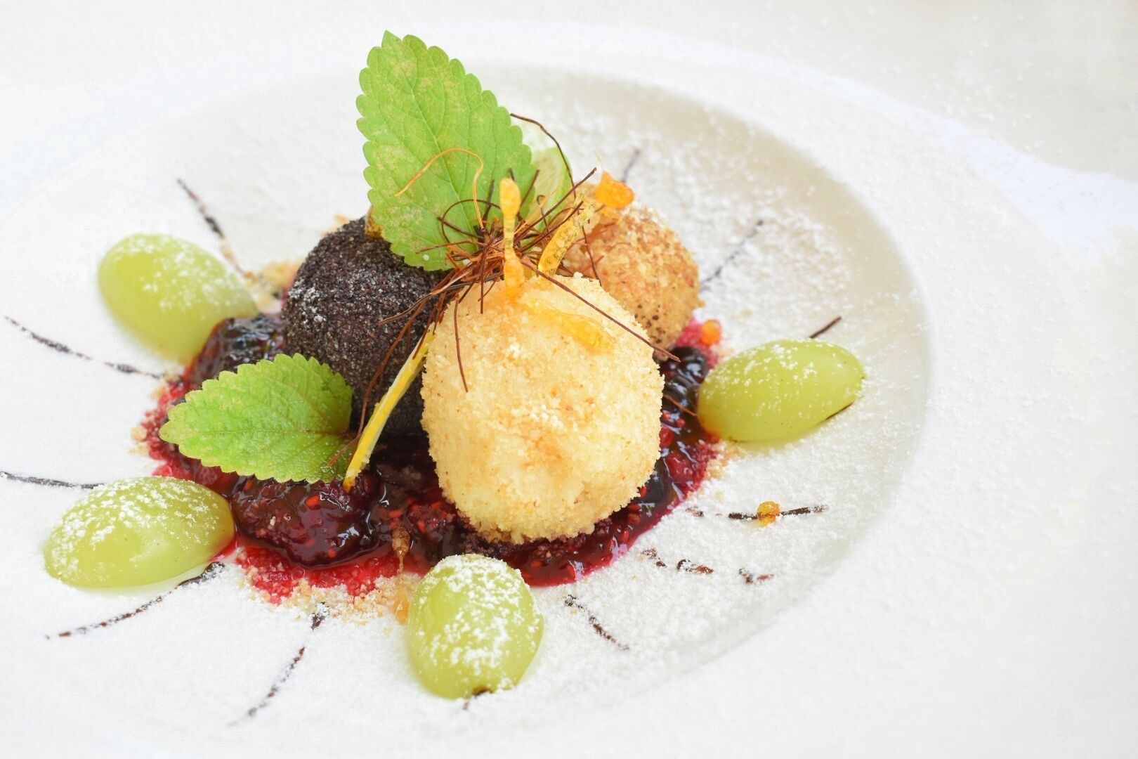 A dessert with a berry compote, a spherical component, and green grapes on a white plate.