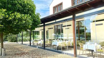 An outdoor dining area with tables and chairs, a tree, and a building with large windows.