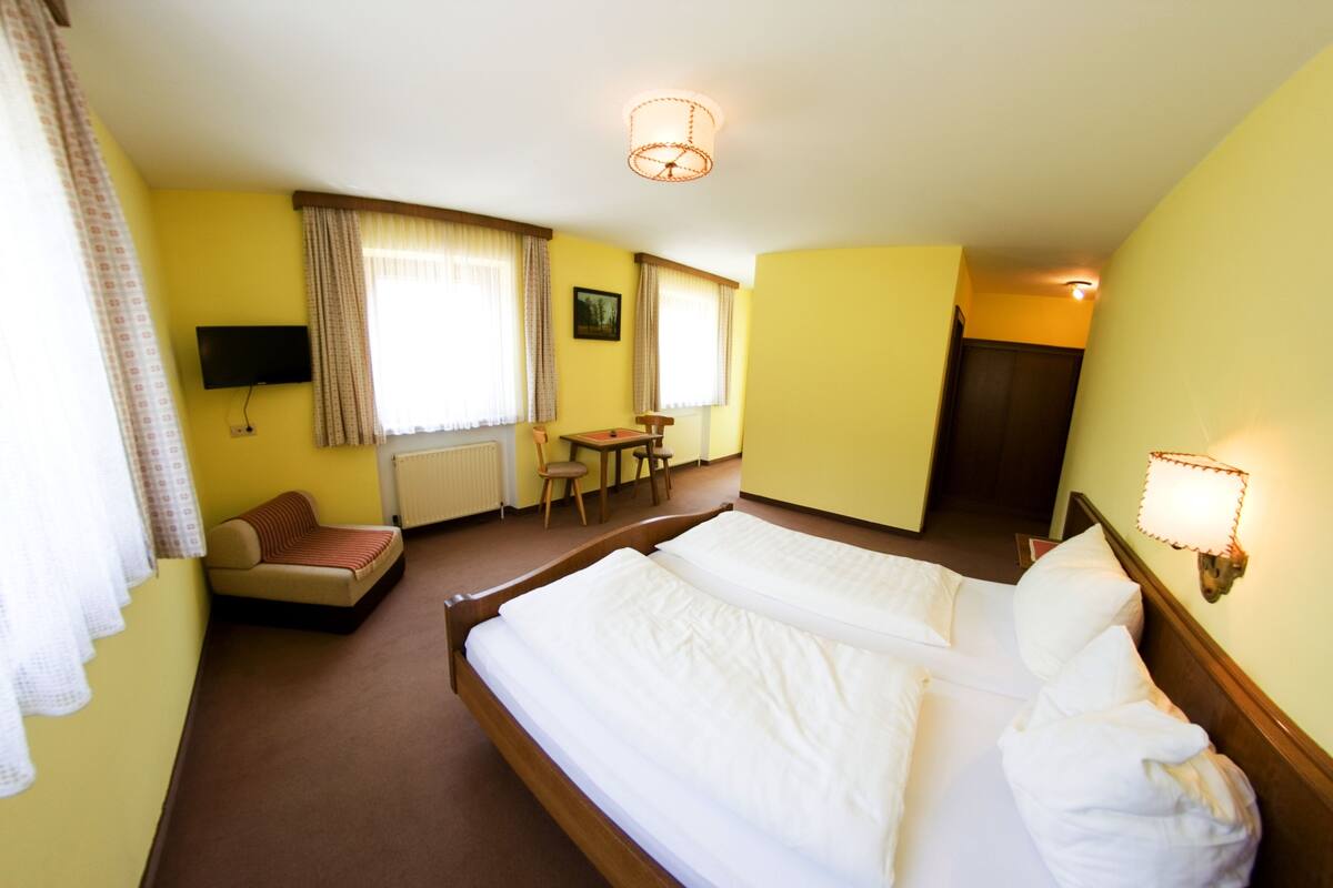 A hotel room with a large bed, a sofa, a small table, and a television.