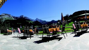 An outdoor seating area with stone flooring, chairs, and tables, surrounded by mountains and a clear sky. - Salzburger Dolomitenhof (Annaberg-Lungoetz)
