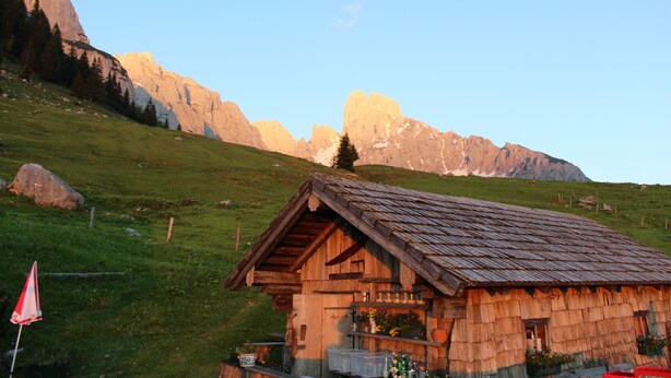 A rustic wooden cabin with a sloped roof, situated on a grassy hillside with mountains in the background. - Salzburger Dolomitenhof (Annaberg-Lungoetz)