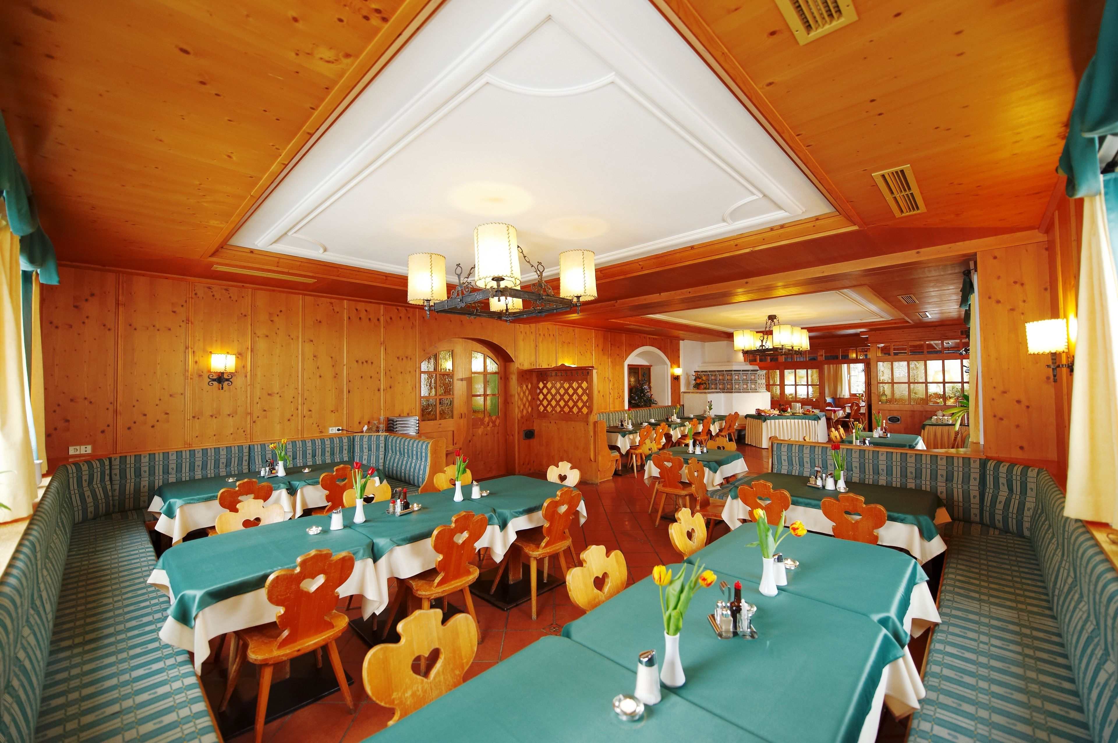 A restaurant with wooden walls and ceiling, multiple tables with green tablecloths, and heart-shaped chairs.