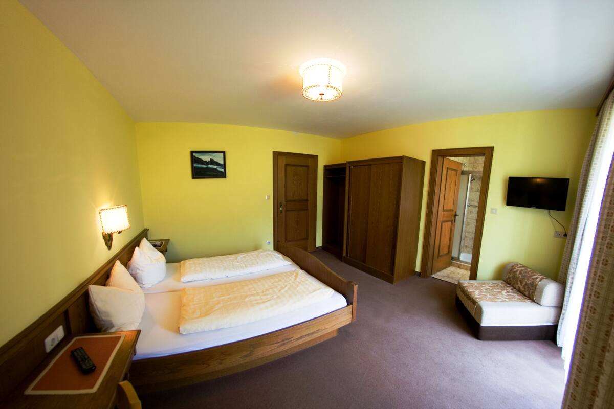 A hotel room with two single beds, a desk with a chair, a TV, and a wardrobe.
