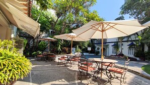 Un patio al aire libre con piso de piedra, mesas, sillas y sombrillas.